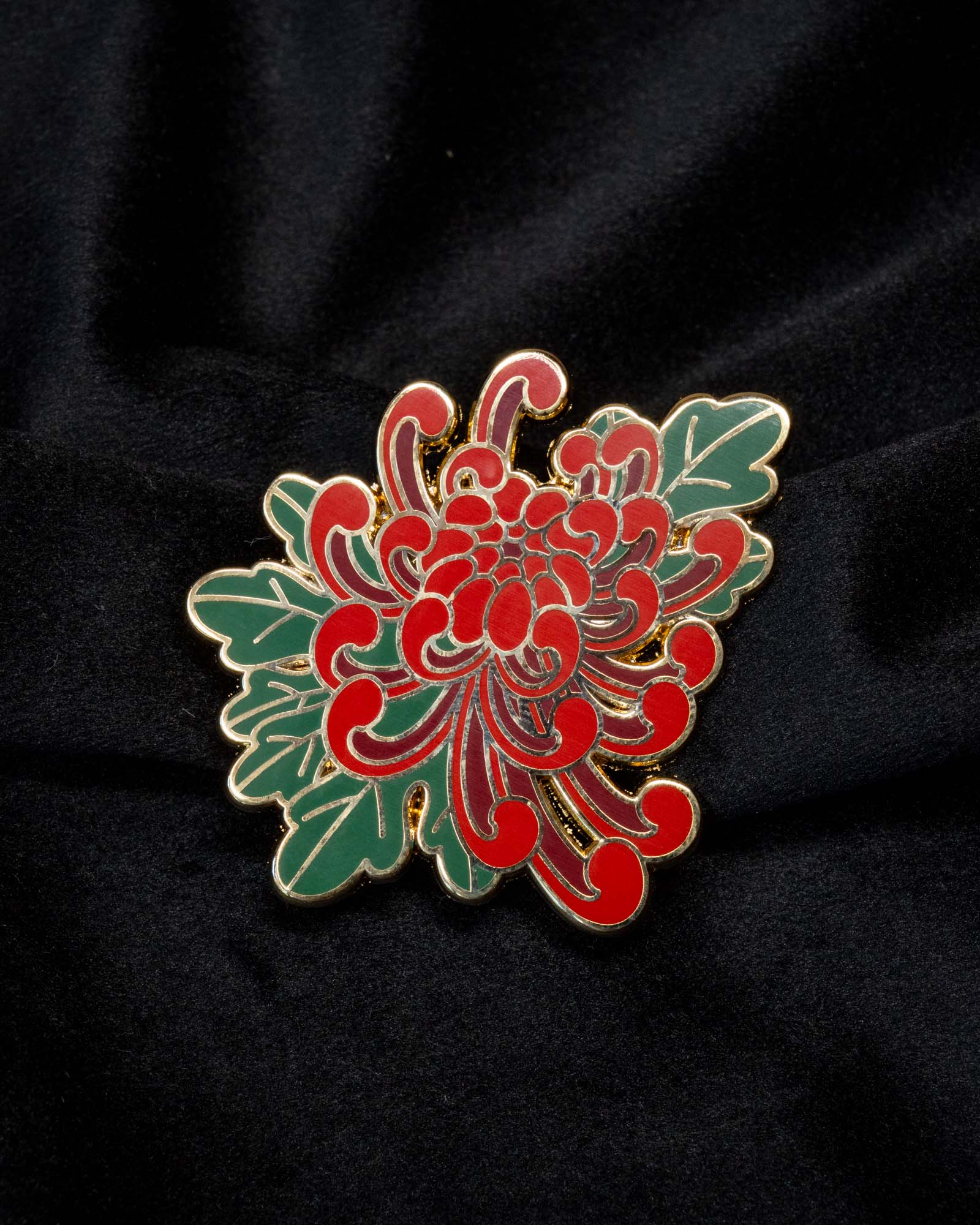 Chrysanthemum enamel pin from the Immovable collection by Geoffrey Wong, featuring a red and green Japanese tattoo-inspired floral design symbolizing renewal and longevity.