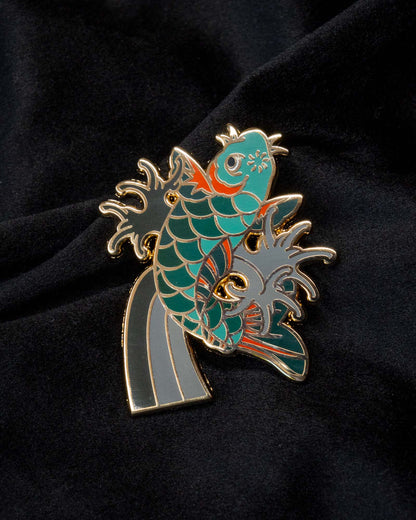Koi enamel pin from the Immovable collection by Geoffrey Wong, showing a vibrant koi swimming upward through waves as a symbol of perseverance and transformation.