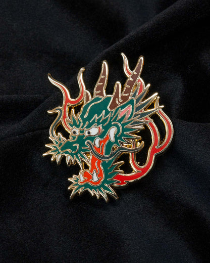 Dragon enamel pin from the Immovable collection by Geoffrey Wong, depicting a green dragon surrounded by flames symbolizing wisdom, power, and protection.