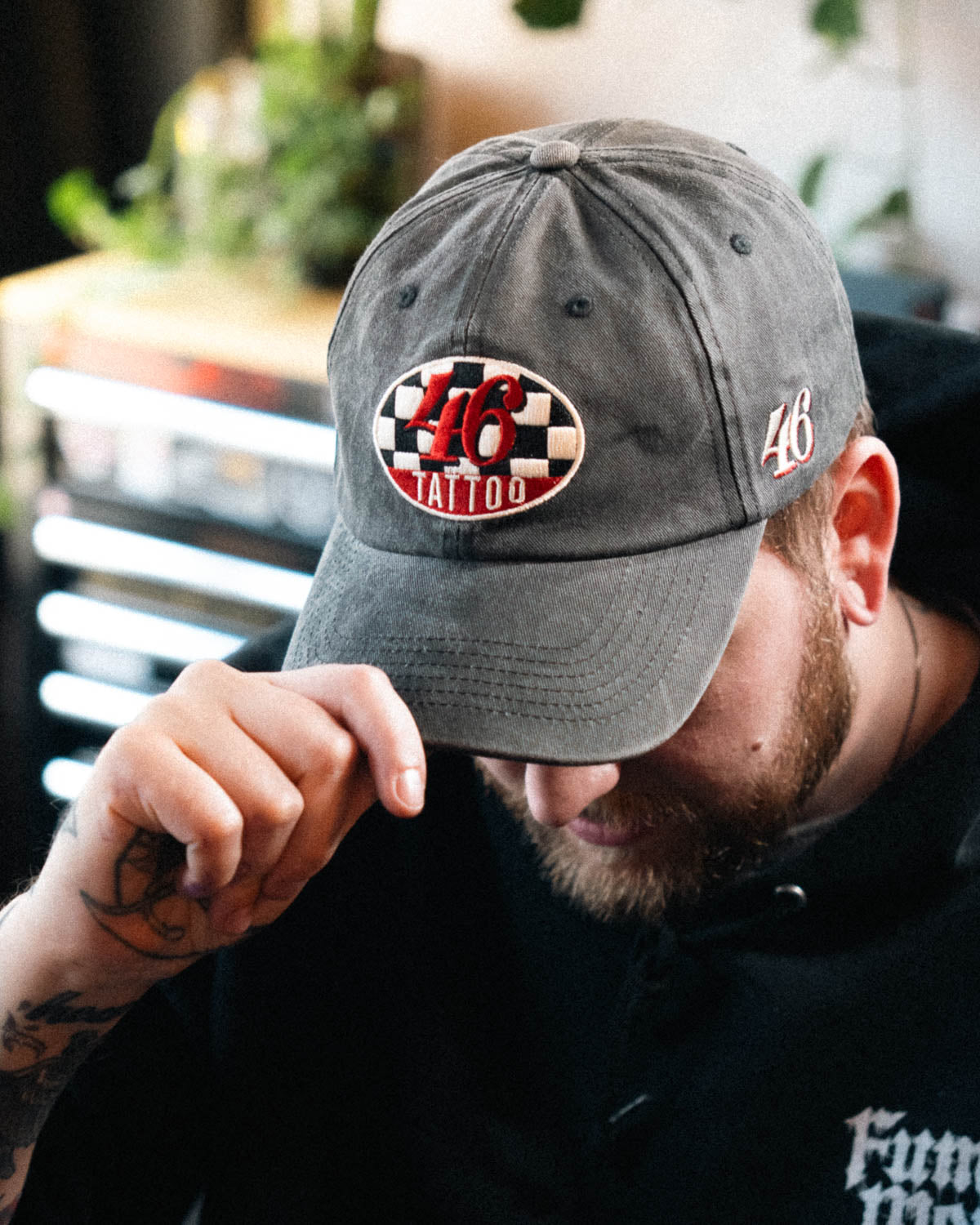 Person wearing a distressed cap, with a 46 tattoo logo, in an indoor setting.