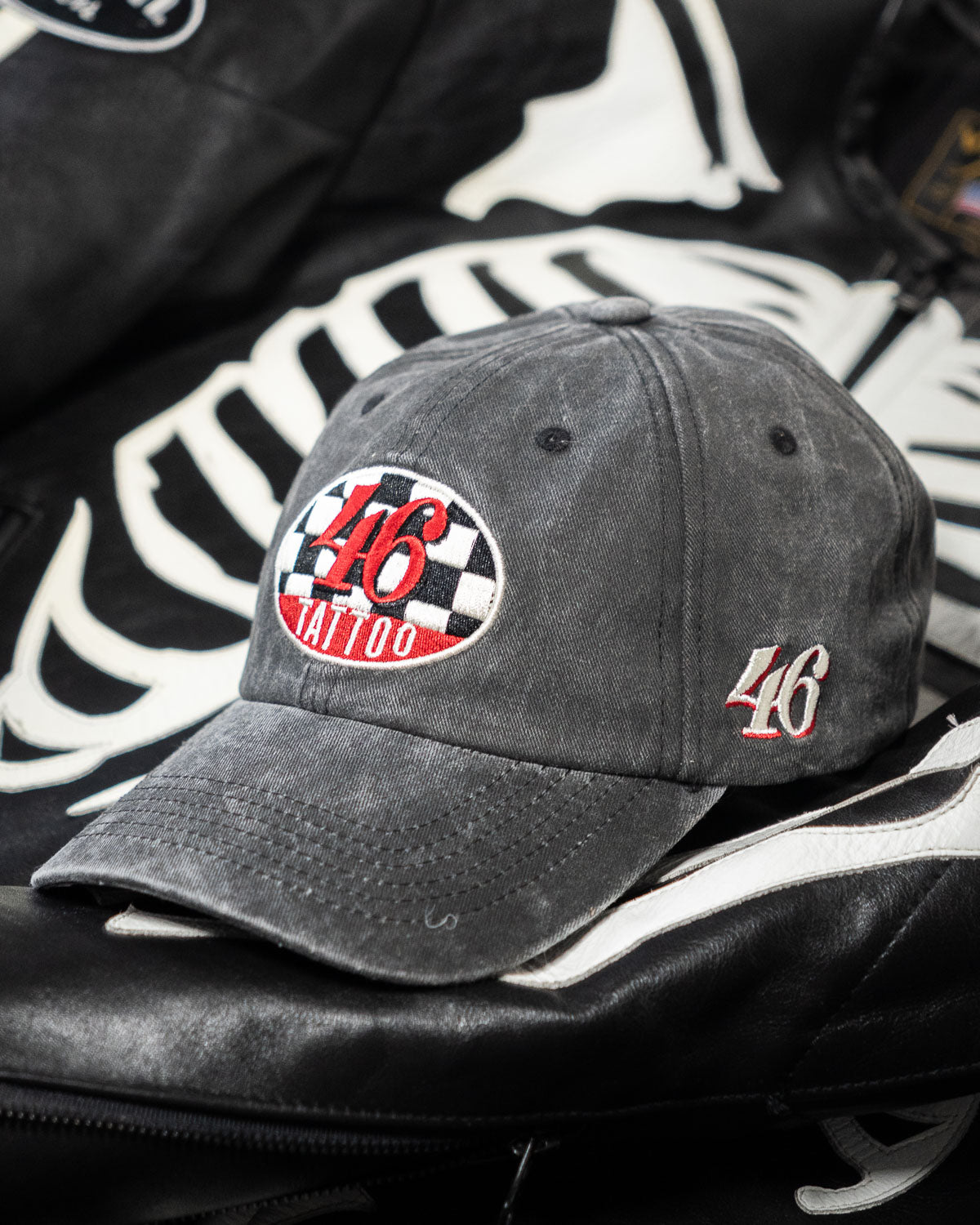 Gray cap with '46 Tattoo' logo on a black jacket with white skeleton design