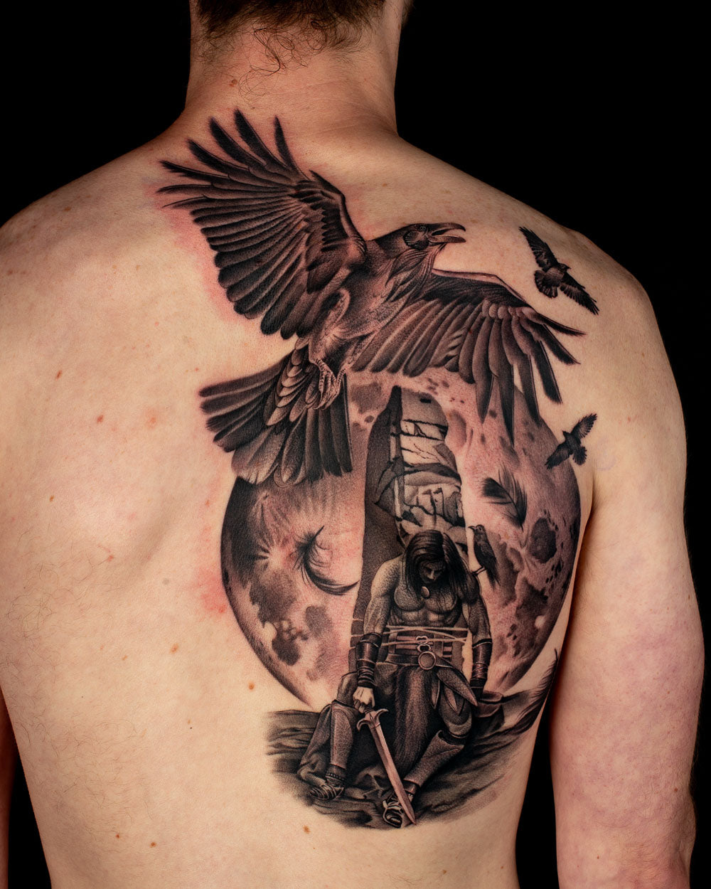 Black and grey realism back tattoo of Cú Chulainn from Irish mythology with ravens and a moon