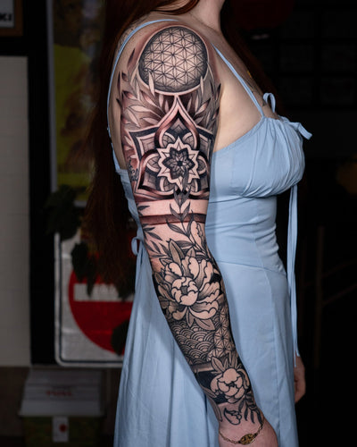 Black and grey ornamental floral and geometric sleeve tattoo with mandala and sacred geometry patterns on the upper arm